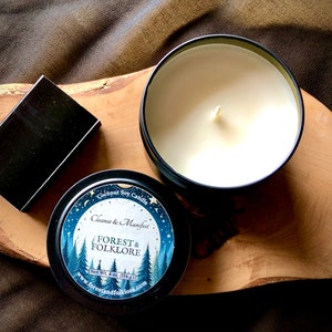 May include: A black tin candle with a white label that says "Coconut Soy Candle Cleanse & Manifest FOREST & FOLKLORE Net Wt. 4 oz. (114g) www.forestandfolklore.com". The label has a blue and white illustration of a forest with a full moon and stars.