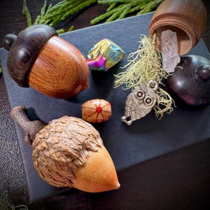 May include: A collection of small wooden acorn-shaped boxes, one open to reveal a clear crystal, along with a small owl charm, a wooden bead with a red and white design, and a iridescent gemstone.