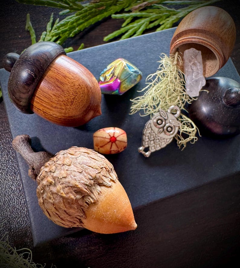 May include: A collection of small wooden acorn-shaped boxes, one open to reveal a clear crystal, along with a small owl charm, a wooden bead with a red and white design, and a iridescent gemstone.