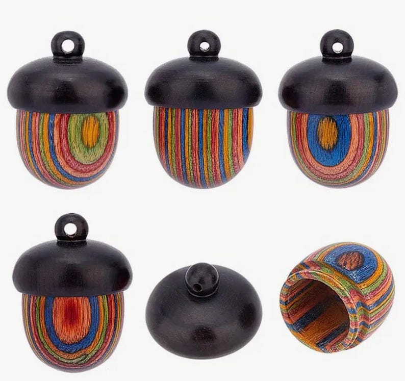 May include: Six wooden acorn-shaped ornaments with colorful striped and circular patterns. The ornaments have a black top and a colorful bottom. One ornament is open to show the inside.