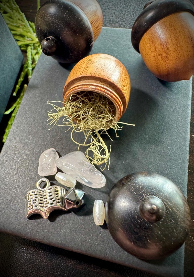 May include: Three wooden acorn-shaped boxes, one open to reveal green moss and clear quartz crystals. A silver charm in the shape of an open book is also visible.