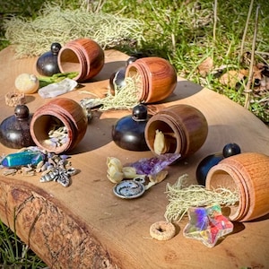 May include: Six wooden acorn-shaped containers with lids, each filled with different natural items, such as crystals, dried flowers, and moss. The containers are arranged on a wooden surface.