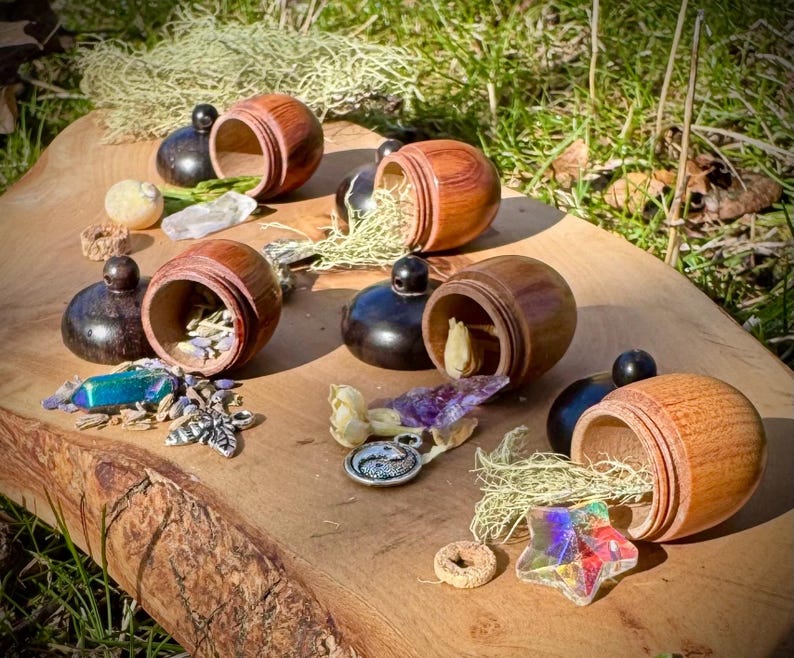 May include: Six wooden acorn-shaped containers with lids, each filled with different natural items, such as crystals, dried flowers, and moss. The containers are arranged on a wooden surface.
