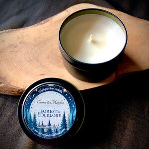 May include: A black metal tin candle with a white label that reads "Coconut Soy Candle, Cleanse & Manifest, FOREST & FOLKLORE, Net Wt. 4 oz. (114 g.), www.forestandfolklore.com". The label features a watercolor illustration of a forest with stars and moons.