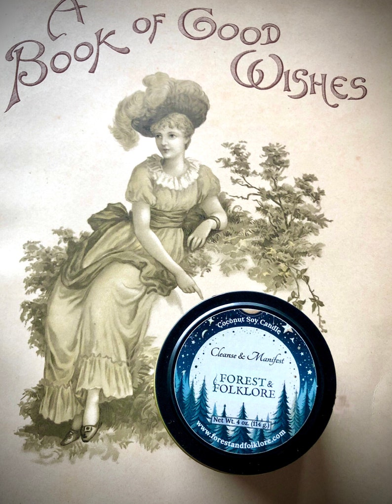 May include: A black tin candle with a blue and white label. The label features a moon, stars, and pine trees. The text on the label reads "Coconut Soy Candle", "Cleanse & Manifest", "Forest & Folklore", "Net Wt. 4 oz. (114 g)", and "www.forestandfolklore.com".