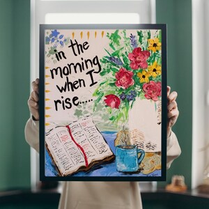 May include: Framed artwork featuring a still life with a vase of red and yellow flowers, a blue mug, and an open book with a red ribbon. The text "in the morning when I rise..." is written on the top left.
