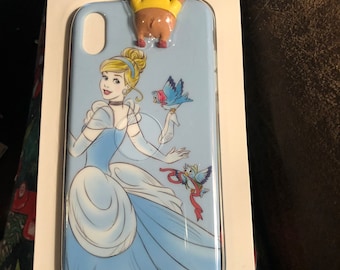 May include: A light blue iPhone XS Max phone case featuring Cinderella in her ball gown with birds. A small figurine of a character is attached to the top. The case is in a white cardboard package with the Disney Parks logo.