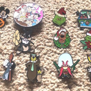 May include: A collection of 14 colorful enamel pins featuring various cartoon characters, including Mickey Mouse, Bugs Bunny, and the Grinch. The pins are all different sizes and shapes, and they are perfect for adding a touch of whimsy to any outfit or bag.