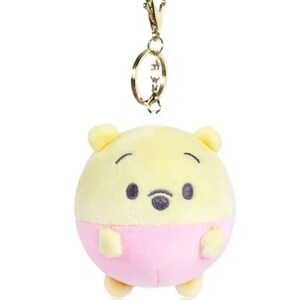 Pode incluir: Um chaveiro de pel&uacute;cia Winnie the Pooh amarelo e rosa. O chaveiro &eacute; redondo e tem um anel de metal dourado.