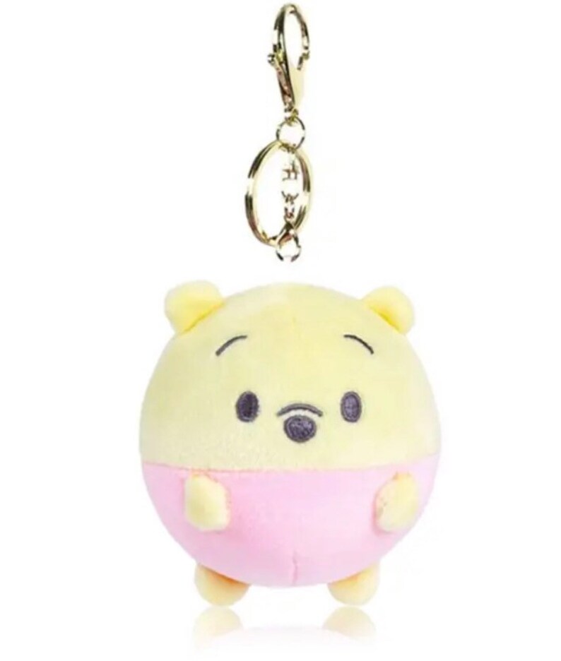 Pode incluir: Um chaveiro de pel&uacute;cia Winnie the Pooh amarelo e rosa. O chaveiro &eacute; redondo e tem um anel de metal dourado.