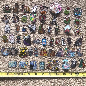 May include: A collection of 50 colorful enamel pins featuring various cartoon characters, including Mickey Mouse, Donald Duck, Goofy, and others. The pins are arranged in rows on a brown carpet-like surface.