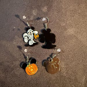 以下が含まれることがあります： ハロウィーンをテーマにした4つのイヤリング。1つのイヤリングは、カボチャのランタンを持っているミイラキャラクターが特徴です。もう1つはキャラクターの黒いシルエットです。3つ目はキャラクターの耳が付いたカボチャです。4つ目は茶色のキャラクターシルエットです。