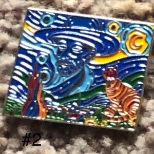 May include: A blue and yellow enamel pin featuring a stylized depiction of Vincent van Gogh's 'Starry Night' painting. The pin includes a self-portrait of van Gogh and a cat in the foreground.