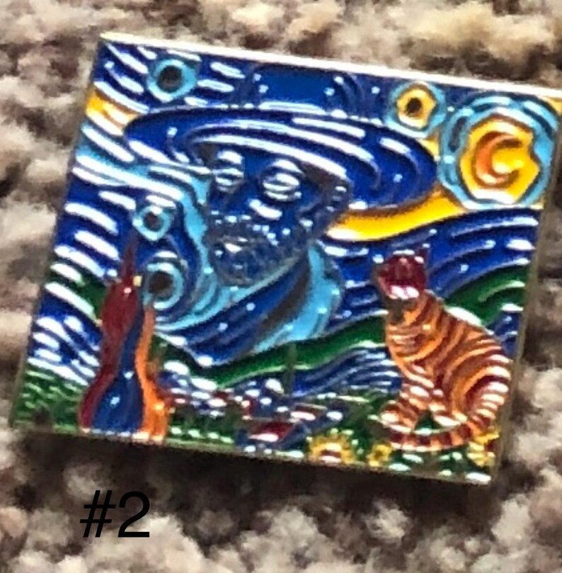 May include: A blue and yellow enamel pin featuring a stylized depiction of Vincent van Gogh's 'Starry Night' painting. The pin includes a self-portrait of van Gogh and a cat in the foreground.