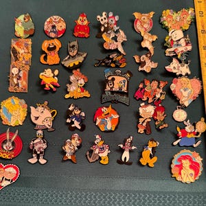 May include: A collection of colorful enamel pins featuring various cartoon characters. The pins include characters from Disney, Looney Tunes, and other animated series. The pins are in various shapes and sizes, with detailed designs and vibrant colors.