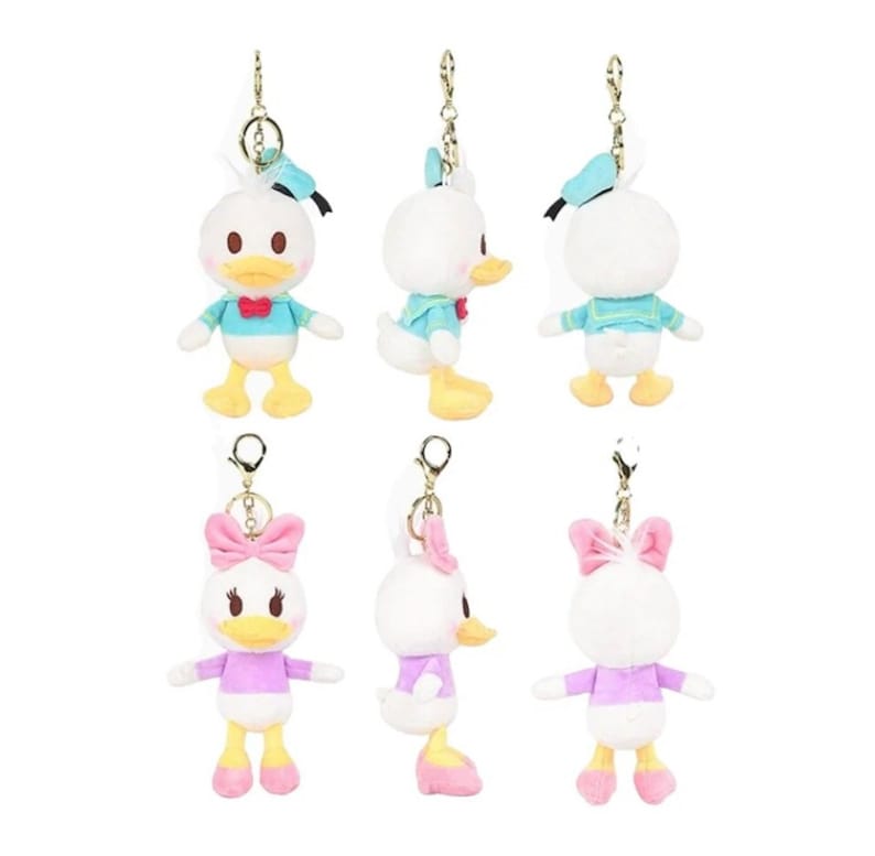 Pode incluir: Seis chaveiros de pel&uacute;cia com os personagens da Disney Donald Duck e Daisy Duck. Os chaveiros est&atilde;o em duas poses diferentes, uma com os personagens olhando para a frente e a outra com os personagens olhando para os lados. Os chaveiros s&atilde;o todos brancos com diferentes acentos de cor. Donald Duck est&aacute; vestindo um traje de marinheiro azul com um bico e p&eacute;s amarelos. Daisy Duck est&aacute; vestindo um vestido roxo com um la&ccedil;o rosa e p&eacute;s amarelos.