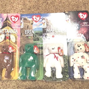 May include: Four Ty Beanie Baby plush toys in their original packaging. The toys are Britannia the Bear, Erin the Bear, Maple the Bear, and Glory the Bear. Each bear is wearing a different country's flag on its chest. The packaging features images of landmarks from each country.
