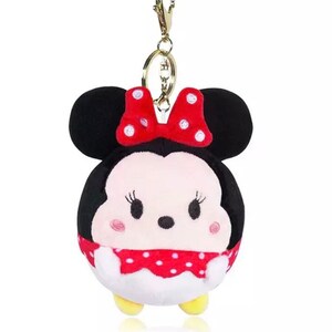 Pode incluir: Um chaveiro de pel&uacute;cia com um personagem de desenho animado com orelhas pretas, um la&ccedil;o vermelho com bolinhas brancas e um rosto branco com olhos pretos e uma boca vermelha. O personagem est&aacute; vestindo um vestido vermelho com bolinhas brancas.