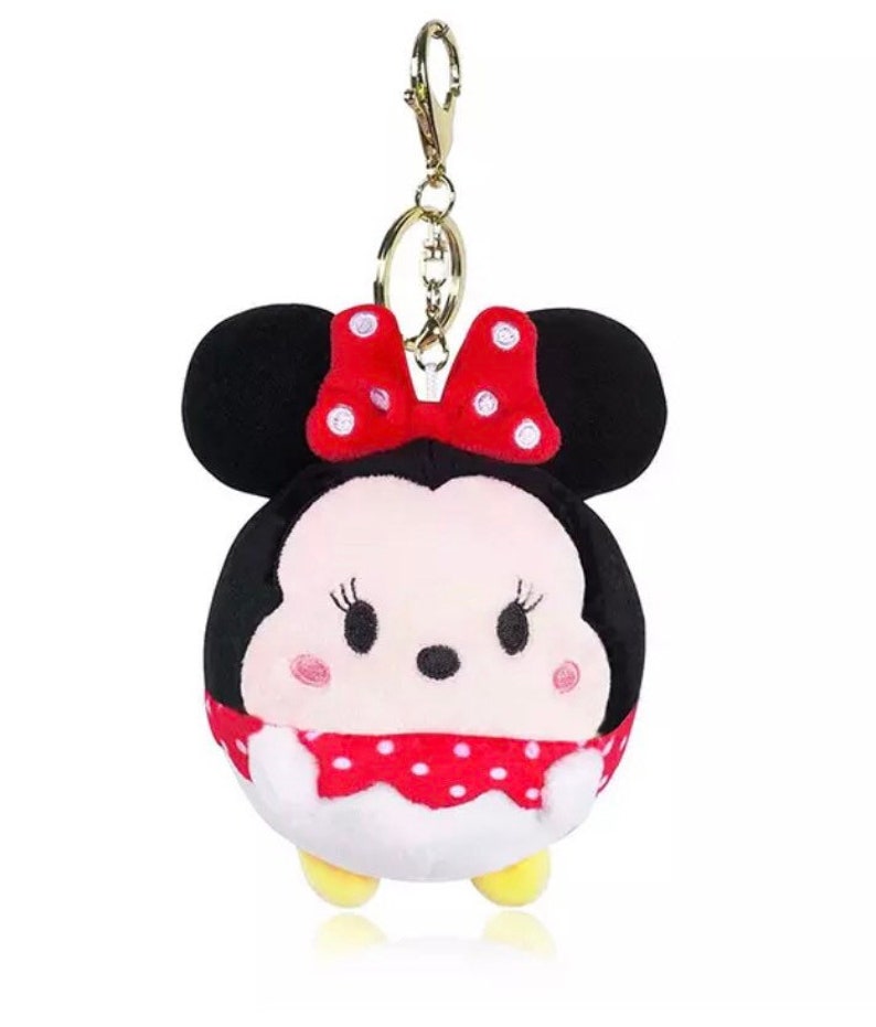 Pode incluir: Um chaveiro de pel&uacute;cia com um personagem de desenho animado com orelhas pretas, um la&ccedil;o vermelho com bolinhas brancas e um rosto branco com olhos pretos e uma boca vermelha. O personagem est&aacute; vestindo um vestido vermelho com bolinhas brancas.