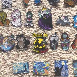 May include: A collection of enamel pins featuring various cartoon and pop culture characters, including a black cat, a cartoon rabbit, a genie, a witch, and a cartoon bird. The pins are colorful and detailed, and they would make a great addition to any fan's collection.