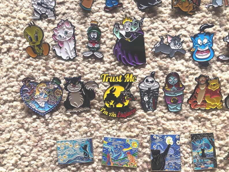 May include: A collection of enamel pins featuring various cartoon and pop culture characters, including a black cat, a cartoon rabbit, a genie, a witch, and a cartoon bird. The pins are colorful and detailed, and they would make a great addition to any fan's collection.