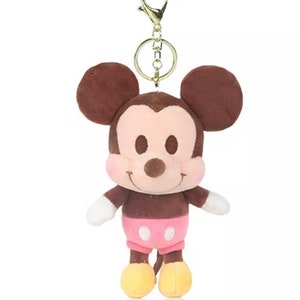 Pode incluir: Um chaveiro de pel&uacute;cia Mickey Mouse marrom com uma camisa de bolinhas rosa e brancas e sapatos amarelos. O chaveiro tem um anel de metal dourado.