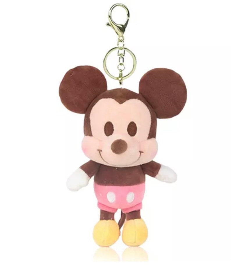 Pode incluir: Um chaveiro de pel&uacute;cia Mickey Mouse marrom com uma camisa de bolinhas rosa e brancas e sapatos amarelos. O chaveiro tem um anel de metal dourado.