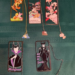 May include: Five rectangular metal bookmarks featuring Disney characters. One shows Tigger and Piglet, one shows Mickey Mouse with the text Experience is the best teacher, one shows Minnie Mouse, one shows Maleficent, and one shows Maleficent with the text Just call me Queen.