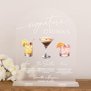 May include: An arched, frosted acrylic sign titled Signature Drinks featuring watercolor illustrations of three cocktails. The text includes John Collins, Espresso Martini, Flamingo Kiss, The Smiths, Samantha & Benjamin, and October 10, 2026.