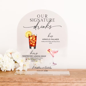 May include: A wedding drink sign with the words "OUR SIGNATURE drinks" in elegant script. The sign features illustrations of two cocktails: an Arnold Palmer and a Raspberry Lemon Drop. The names of the couple and the wedding date are also displayed.
