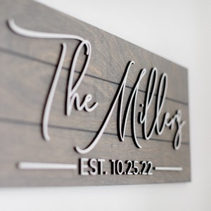 May include: A wooden sign with the text "The Millers - EST. 10.25.22" in white raised lettering.