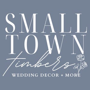 May include: A logo on a dusty blue background featuring the white text SMALL TOWN in a serif font, followed by the word Timbers in a white script font, and the text WEDDING DECOR + MORE below. A white line drawing of two roses is on the right.