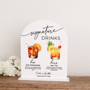 May include: An arched white sign featuring the text Signature Drinks, with illustrations of an Old Fashioned and a Mai Tai. Below the drinks, the text reads his Old Fashioned, hers Mai Tai, Caroline & Jonathan, and September 19, 2026.
