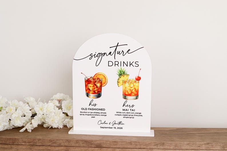 May include: An arched white sign featuring the text Signature Drinks, with illustrations of an Old Fashioned and a Mai Tai. Below the drinks, the text reads his Old Fashioned, hers Mai Tai, Caroline & Jonathan, and September 19, 2026.
