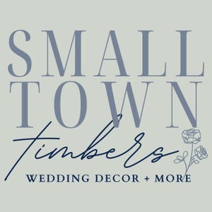 May include: A graphic logo on a light gray background featuring the text SMALL TOWN in large blue serif letters, the word Timbers in a dark blue script font, and the text WEDDING DECOR + MORE below, accompanied by a small line-art floral illustration.