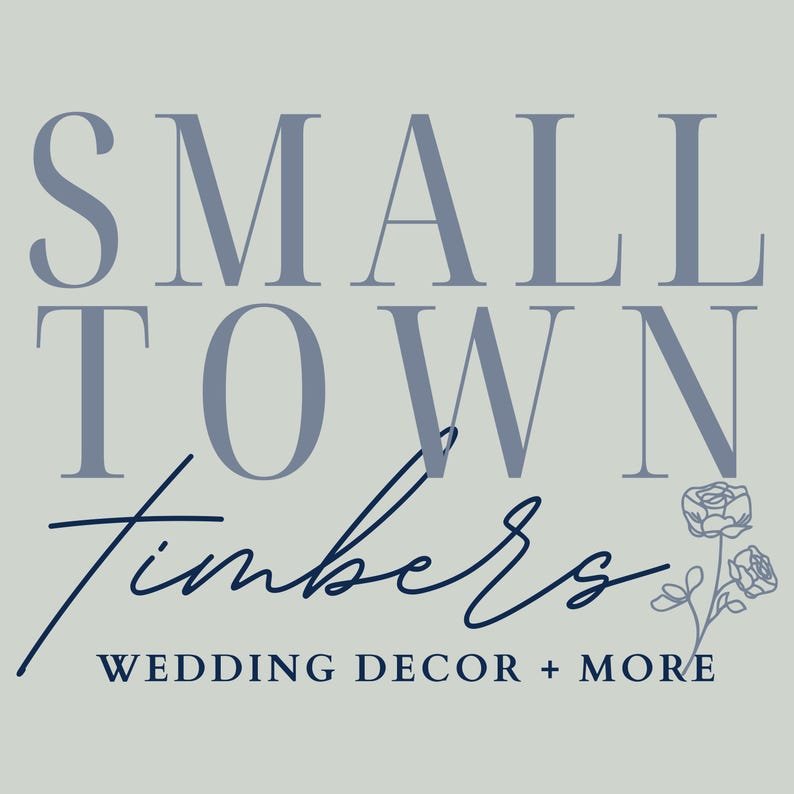 May include: A graphic logo on a light gray background featuring the text SMALL TOWN in large blue serif letters, the word Timbers in a dark blue script font, and the text WEDDING DECOR + MORE below, accompanied by a small line-art floral illustration.