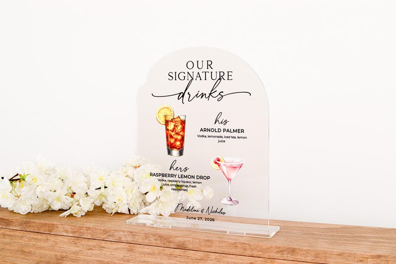 May include: An arched clear acrylic sign featuring the text "OUR SIGNATURE drinks" with illustrations of an Arnold Palmer and a Raspberry Lemon Drop cocktail. The sign lists ingredients for each drink, the names "Madeline & Nicholas", and "June 27, 2026".