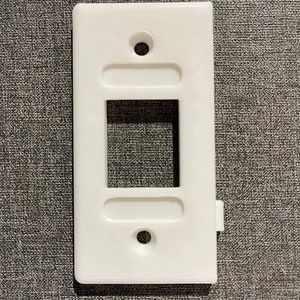 May include: White plastic wall plate with a rectangular cutout for a light switch or outlet. The plate has two small round holes at the top and bottom.