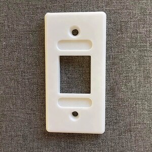 May include: White plastic wall plate with a rectangular cutout for an electrical outlet or switch.