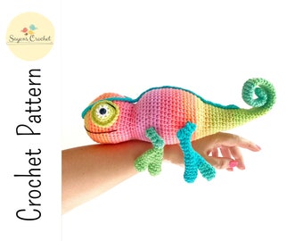 May include: A crocheted chameleon toy with a rainbow gradient color scheme. The chameleon has a green tail, turquoise legs, and a pink body with a yellow eye.