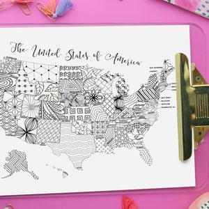 Printable coloring page map of the USA, with text along the top that reads, The United States of America. Each state is labeled and has a different, intricate design. The map is displayed on a clipboard on a pink background.