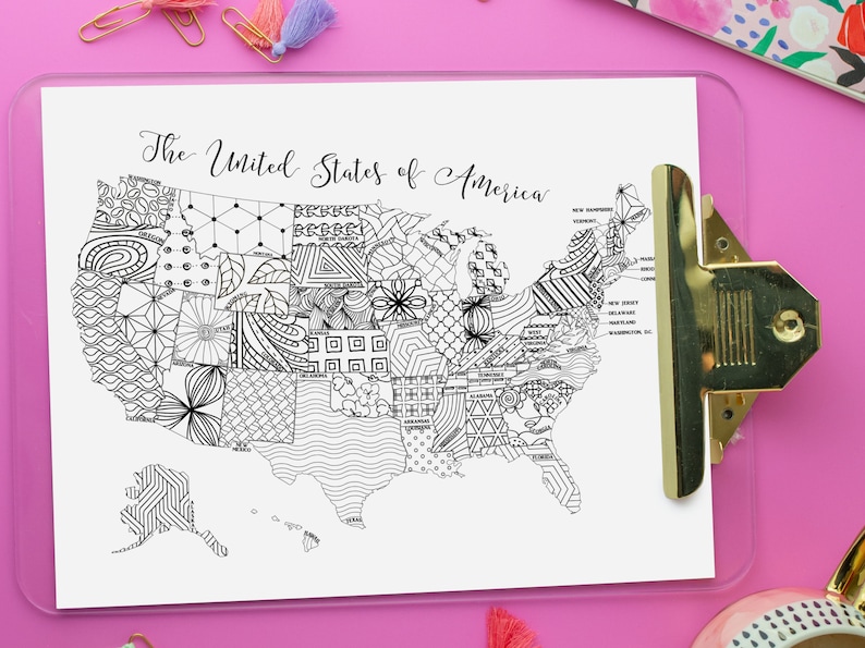 Printable coloring page map of the USA, with text along the top that reads, The United States of America. Each state is labeled and has a different, intricate design. The map is displayed on a clipboard on a pink background.