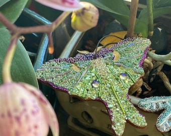 May include: A green and purple beaded moth ornament with iridescent wings. The moth is made of small beads and sequins and has a detailed design.