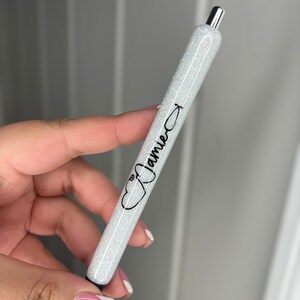 May include: A white glitter pen with a silver top and black ink. The pen has a stethoscope symbol and the name "Jamie" printed on it.