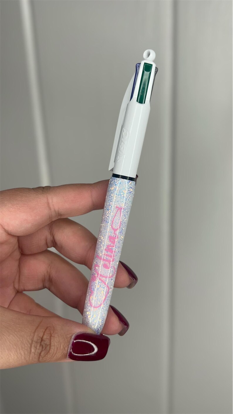 May include: A white pen with a glittery finish and pink lettering that says "Mom". The pen has a green, blue, and black ink cartridge.