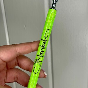 May include: A bright green glitter pen with a silver top and a black heart with the word "Maybelline" written inside.