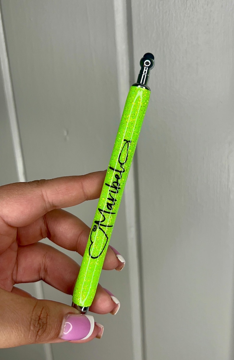 May include: A bright green glitter pen with a silver top and a black heart with the word "Maybelline" written inside.