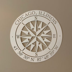 May include: White metal compass with a star design and the text "CHICAGO, ILLINOIS" and coordinates "41° 58' 30" N 87° 48' 59" W".