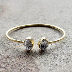 May include: A gold bangle bracelet with two clear, faceted, rough-cut diamond-shaped stones.