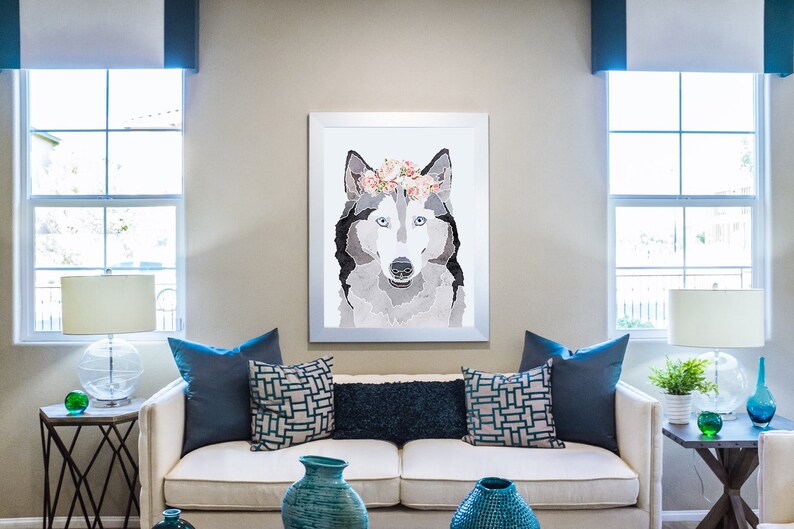 May include: A white couch with blue throw pillows in a living room setting. A framed print of a wolf wearing a flower crown hangs on the wall above the couch.